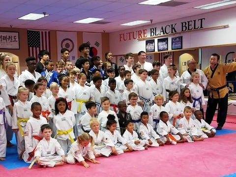 Group of children and adults in martial arts uniforms at a karate dojo with Future Black Belt sign visible