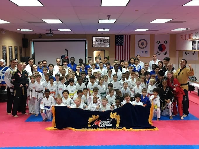 Large group of martial arts students in white and colored uniforms posing together on a pink mat during a taekwondo class photo